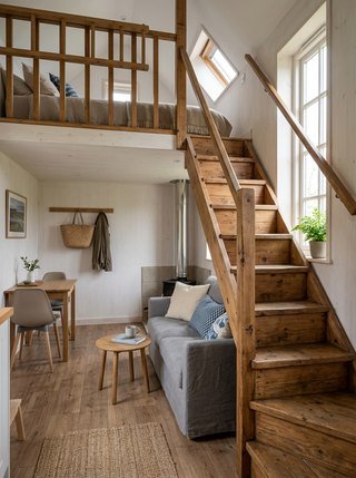 Staircase leading to a loft in a Scandinavian tiny house, naturally lit by a tall, narrow window